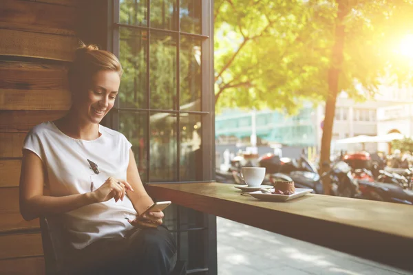 Glückliche Kaukasierin sieht ihr Foto auf dem Handy, während sie sich in der Freizeit im Café entspannen — Stockfoto