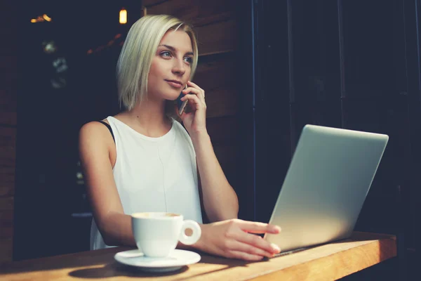 Blonde vrouwelijke freelancer praten op mobiele telefoon tijdens het werk op draagbare laptop computer — Stockfoto