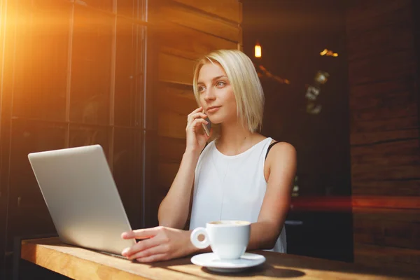 Blonde Kaukasierin telefoniert während der Arbeit am tragbaren Laptop — Stockfoto