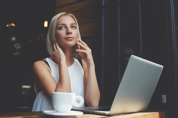 Mulher loira bonita chamando no telefone celular enquanto descansa após o trabalho no computador portátil — Fotografia de Stock