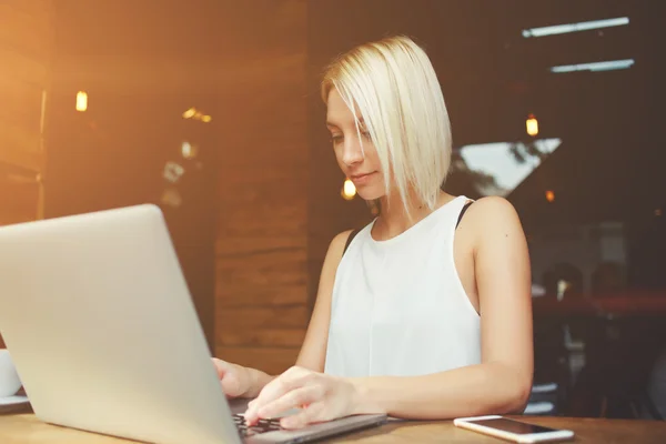 Freelancer mulher loira bonita usando net-book para trabalho à distância durante café da manhã no café — Fotografia de Stock