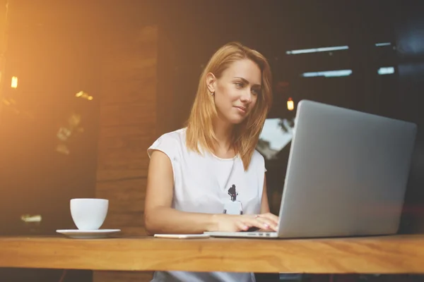 Freelancer feminino bem sucedido usando net-book para trabalho à distância durante café da manhã no café — Fotografia de Stock