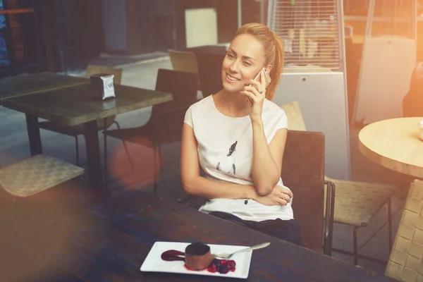 Mujer bastante feliz llamando con teléfono inteligente durante el desayuno de la mañana en la cafetería — Foto de Stock