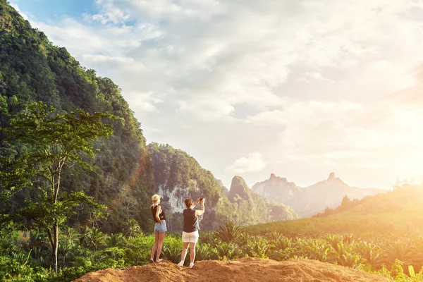 Дві жінки роблять фотографії на мобільному телефоні, в той час як стоїть на тлі джунглів і хмарного неба з копіювальним простором — стокове фото