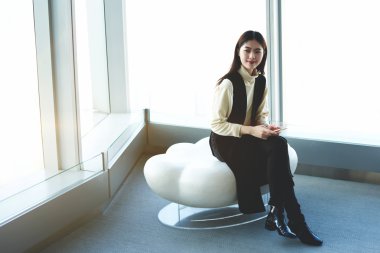 Young Japanese businesswoman with mobile phone in hands is waiting international partners in airport hallway 