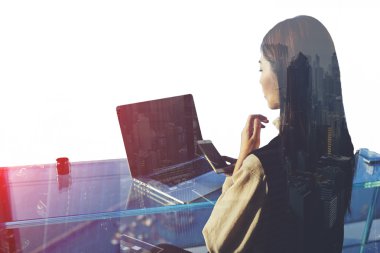 Başarılı iş kadını cep telefonundan kısa mesaj okurken, boş kopya alan ekranı ile açık net kitap önünde oturuyor 