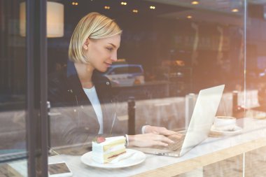 Young female is sending files via net-book during breakfast in modern coffee shop