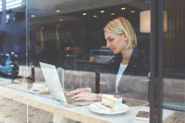 Young hipster girl is working on net-book, while is sitting in modern hipster coffee shop interior