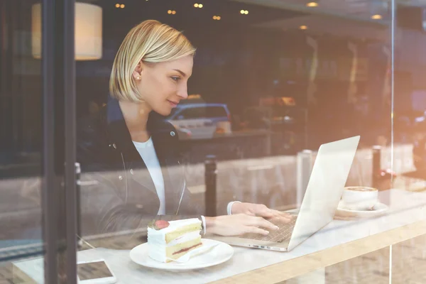 Young female is sending files via net-book during breakfast in modern coffee shop — Stok fotoğraf