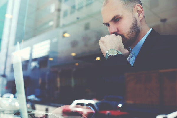 Confident businessman with serious face is using net-book during coffee break 