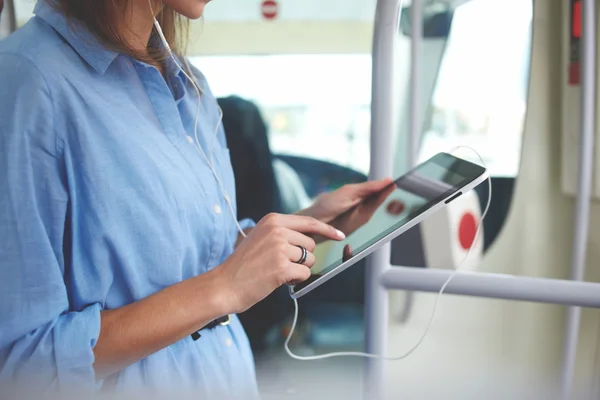 Étroitement de la jeune fille hipster écoute de la musique via un casque sur le pavé tactile portable, tandis que monte dans un bus . — Photo