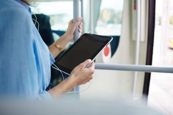 Ściśle obrazu hipster młoda dziewczyna z słuchawki jest oglądanie wideo w sieci społecznej poprzez panel dotykowy, podczas gdy stoi w transporcie publicznym — Zdjęcie stockowe