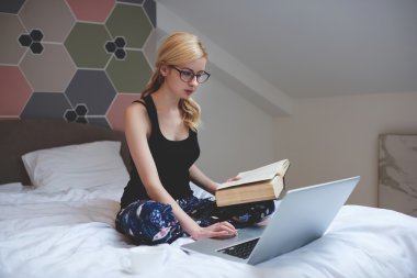 Gözlüklü şirin kız öğrenci çalışması malzeme internet dizüstü bilgisayar, ev iç otururken arıyor