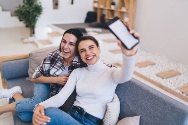 Arkadaşlarıyla kanepede oturup sosyal medyada komik yazılar okurken kameraya mobil ekran gösteren pozitifler.