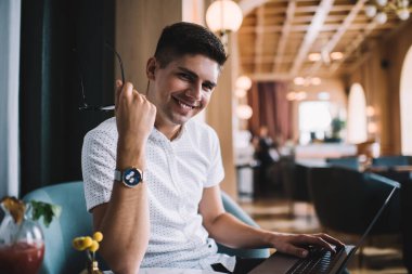 Laptop projesinde çalışan mutlu genç erkek ve kafede oturmuş kameraya bakarken gülümsüyor.