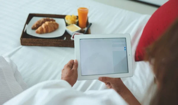 From below crop of unrecognizable person resting with laptop and eating croissants while lying on bed at home in Hong Kong