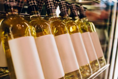 Beyaz şarapla dolu aynı kapalı cam şişeler vitrinde raflara dizilmiş bardaki camlar aracılığıyla.