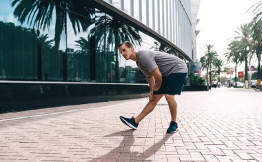 Güçlü beyaz erkek koşucu ısınma egzersizleri yapıyor. Sokaklarda kaslarını esnetiyor, sporcu aktif olarak antrenman yapıyor. Sağlıklı yaşam tarzını, yaşam tarzını ve sağlığını korumaya odaklanıyor.