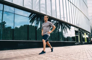 Beyaz erkek koşucu, şehir merkezinde çömelmiş, sabahki yaya geçidinde yoğunluk antrenmanının keyfini çıkarıyor. Spor kıyafetleri içindeki kararlı adam, sokakta egzersiz yaptığı için vücudunu ısıtıyor.