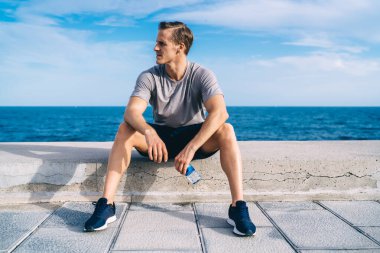 Düşünceli beyaz erkek koşucu. 30 yaşında. Su dolu barajda dinleniyor. Aktif giyinen aktif sporcu antrenmanı bitirmeyi düşünüyor.