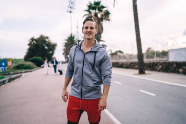 Gülümseyen beyaz tenli sporcunun yarı boy portresi aktif giyinmiş şehir ortamında poz veren yakışıklı erkek koşucu 20 yaşında kameraya bakıyor zindeliğin ve sağlıklı yaşam tarzının tadını çıkarıyor.