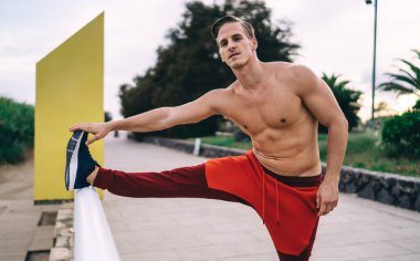 Güçlü erkek antrenör. 20 'li yaşlarda. Sabah antrenmanı sırasında vücut kaslarını esnetiyor. Karın kasları şişmiş üstsüz sporcu.