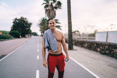 Antrenman sırasında kameraya üstsüz gülümseyen başarılı sporcunun yarım boy portresi kaslarını çalıştırmak için mükemmel vücut şekline sahip, fiziksel ısınmaya hazır poz veren sporcu.