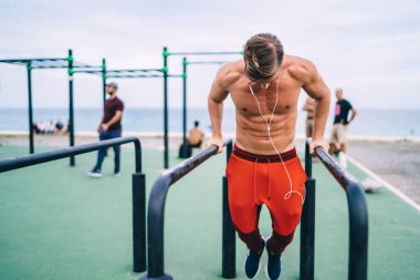 Beyaz tenli güçlü sporcu açık hava barlarında egzersiz yapıyor elektronik kulaklıkla müzik dinliyor ve sağlıklı yaşam tarzını koruyor üstsüz erkek vücut geliştirici vücut kaslarını ve vücut şeklini eğitiyor.