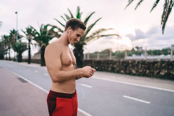 快乐的白人运动员与性感的身体使用手机媒体应用程序收听音乐播客 成功的裸体健美者的消息 博客追随者写体育答案 — 图库照片