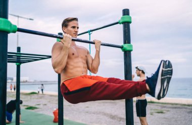 Güçlü beyaz erkek sporcu dışarıda antrenman yapıyor kas gücünü ve canlılığını koruyor, mükemmel vücutlu üstsüz sporcu sokak sporu yapıyor hedeflere ulaşmak ve egzersiz yapmak için parmaklıkları kullanıyor.