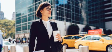 Beyaz bluzlu ve siyah takım elbiseli başarılı bayan girişimci New York 'taki modern binalara karşı gazete ve kahve taşıyor.