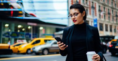 Siyah takım elbiseli kadın yoğun yolun kenarında duruyor ve New York 'un caddesinde telefonla mesajlaşıyor.