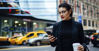 Siyah takım elbiseli kadın yoğun yolun kenarında duruyor ve New York 'un caddesinde telefonla mesajlaşıyor.