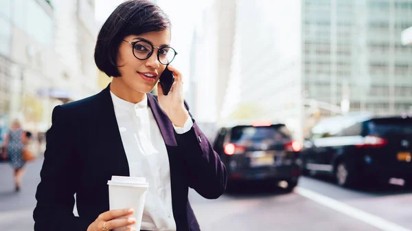 路上に立ちスマートフォンで話すテイクアウトコーヒーのカップと正式な摩耗や眼鏡のエレガントな民族経営の女性 — ストック写真