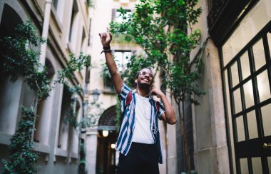 Pozitif Afro-Amerikan hipster melodisi kulaklıklarda mükemmel bir sesle heyecanlanan, şehirde müzik eşliğinde dans eden, cep telefonu çalma listesindeki yeni şarkılarla tatmin olmuş koyu tenli bir erkek.