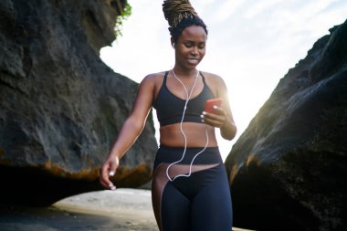 Düşük açılı Afrika kökenli Amerikalı sporcu, kulaklıkla müzik dinlerken gülümseyen ve mesajlaşan aktif giyimli.