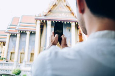 Cep telefonu kullanan erkek gezginlerin arka planı, altın tapınağın resmini Asya dinini keşfetmek, akıllı telefon kamerasıyla video çeken bir blogcu, Tayland 'ı ziyaret eden ve yer belirleyen
