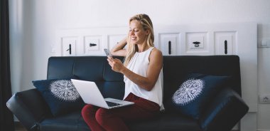 Netbook aygıtı üzerinde çalışırken cep telefonuyla mesajlaşmaktan keyif alan mutlu Kafkasyalı serbest yazar, iletişim uygulaması kurulumu için mobil bildirimi kontrol eden zengin kadın kullanıcı