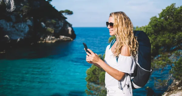 Happy travel blogger holding modern cellphone device for creating influence content and share to social websites, carefree Caucasian tourist enjoying summer vacations for exploring Menorca island