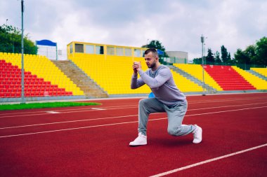 Spor giyim sektöründe uzun boylu kaslı sporcunun antrenman sırasında sahada durup esneme egzersizleri yapmasının yan görüntüsü.