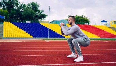 Stadyumda Tribün 'e karşı atlama egzersizleri yaparken eşofmanlı ve spor ayakkabılı kararlı güçlü antrenörün yan görüntüsü.