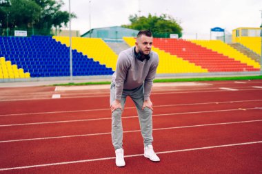 Eşofmanlı, kulaklıklı, stadyum pistinde dinlenen ve gözlerini kaçıran bir sürü konsantre genç adam.