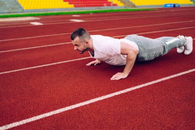 Zayıflamak ve mükemmel vücut şekline ulaşmak için stadyum antrenmanlarında şınav çeken ciddi güçlü beyaz erkek, genç 20 'li yaşlarda kararlı sporcu sabahları kardiyo antrenmanlarına hazırlanıyor.