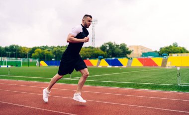 Hareketli yakışıklı adam stadyumun dışında koşuyor. Esneklik ve hedeflere ulaşmak için koşuyor. 20 'li yaşlarda erkek koşucu formda ve formda kalmak için sabah antrenmanı yapıyor.