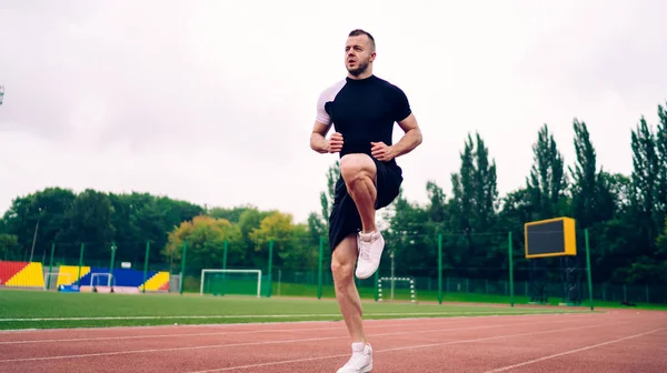 Positive caucasian male in activewear raising legs prepare for running spring on stadium,strong determined young man jogger training for spring and marathon enjoying healthy lifestyle and body
