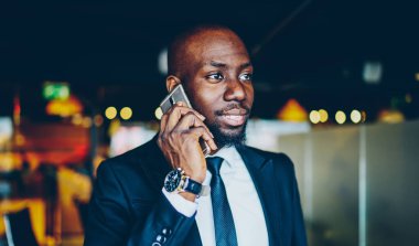 Resmi giyinmiş koyu tenli iş adamı operatöre telefon etmek için cep telefonu uygulaması kullanıyor. Elinde İsviçre saati olan Afrikalı Amerikalı şirket müdürü cep telefonuyla danışmanlık görüşmesi yapıyor.