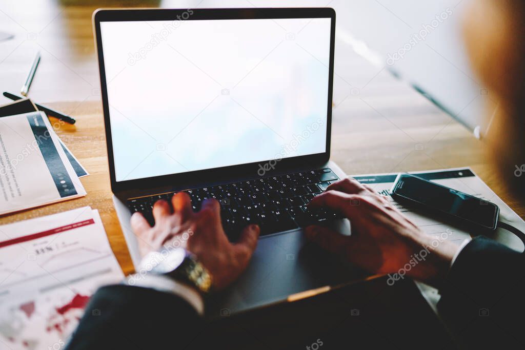 Cropped male entrepreneur using mockup laptop for analyzing online investment connected to office internet, experienced businessman browsing information on blank netbook with copy space area