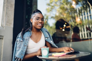 Yarım boy, esmer, şık giyinmiş, cafe terasında kahve molası veren, gözlüklü, 20 'li yaşlarda Afro-Amerikan hippi bir kızın fotoğrafına.