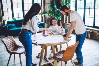 Beyaz tişörtlü neşeli çok ırklı iş arkadaşları iş detaylarını anlatırken ofiste kahve içmek ve kağıtları analiz ederken...