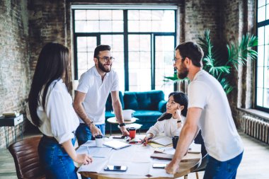 Erkek ve kadın yöneticiler pazarlama stratejisini tartışırken aynı zamanda tuğla duvarlar ve panoramik pencerelerle gün ışığında birlikte çalışıyorlar.